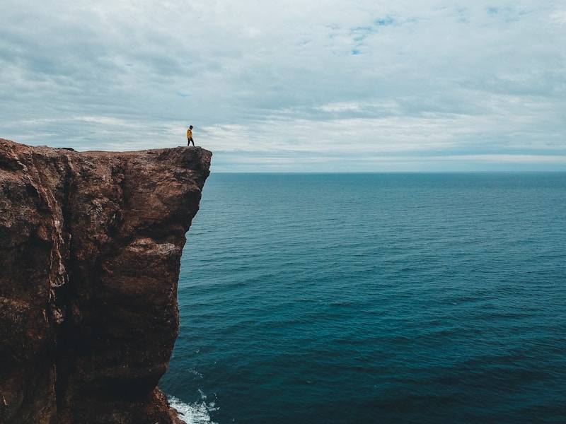 Person in a yellow jacket standing on a cliff edge overlooking the ocean
